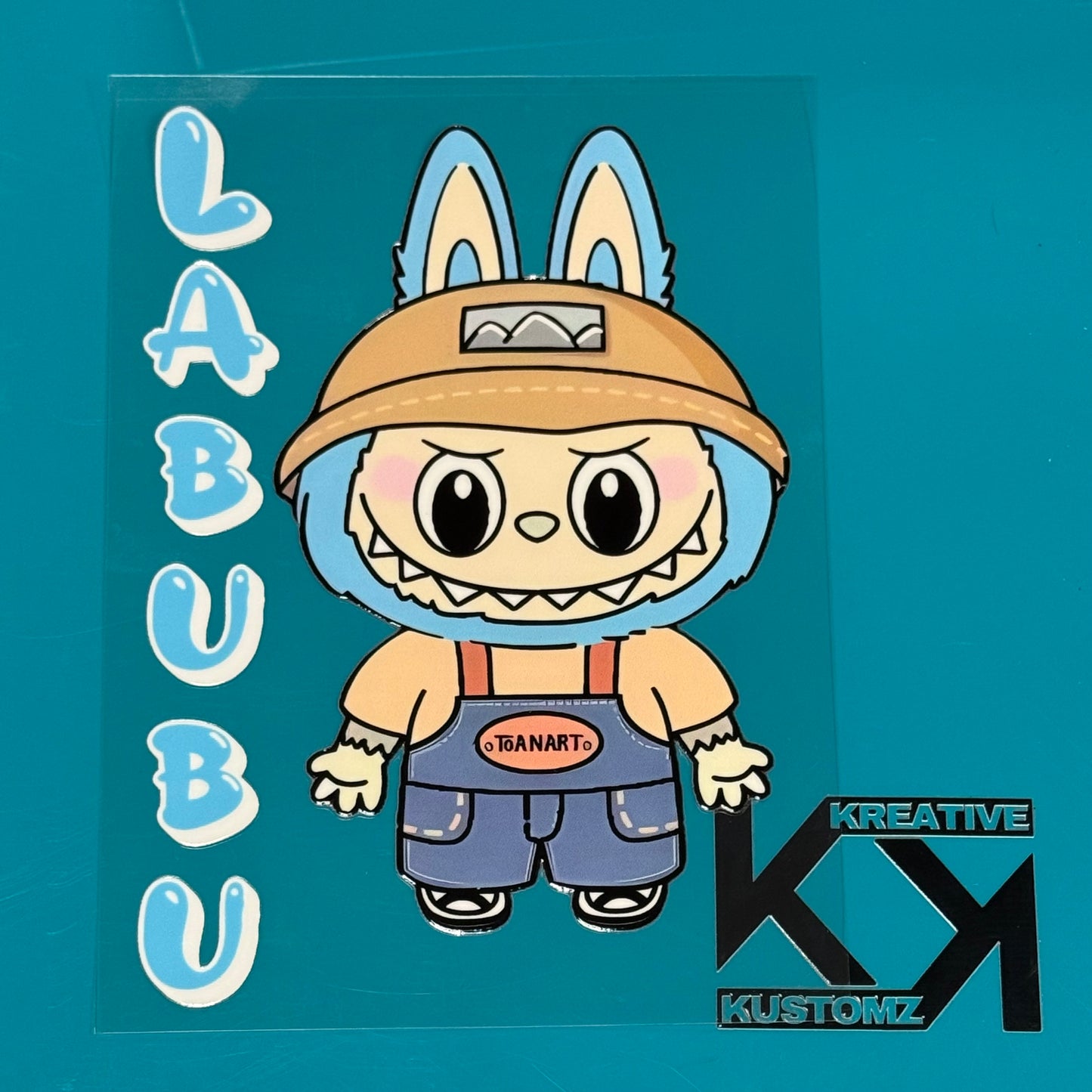 A Labubu character sticker with blue fur and overalls on a clear backing with text accents.