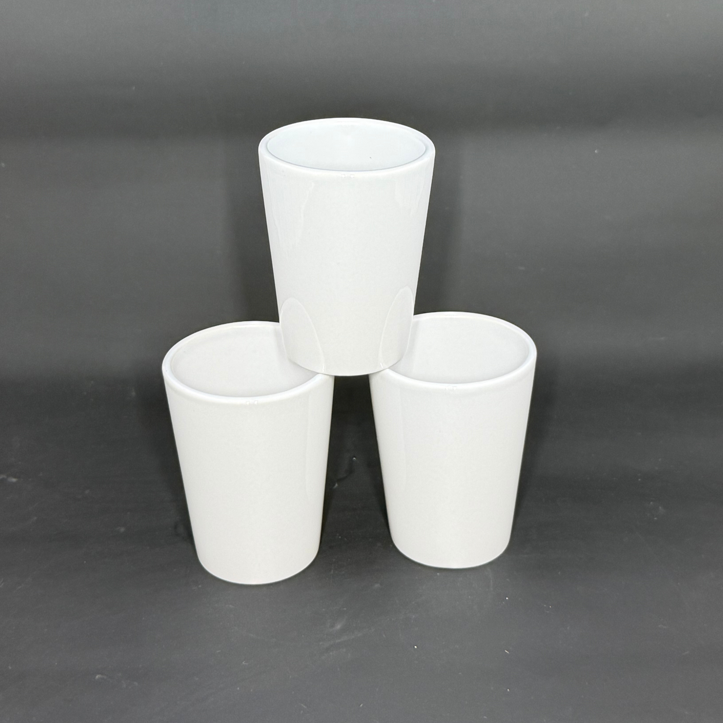 Three white ceramic shot glasses are arranged in a pyramid formation against a dark background.