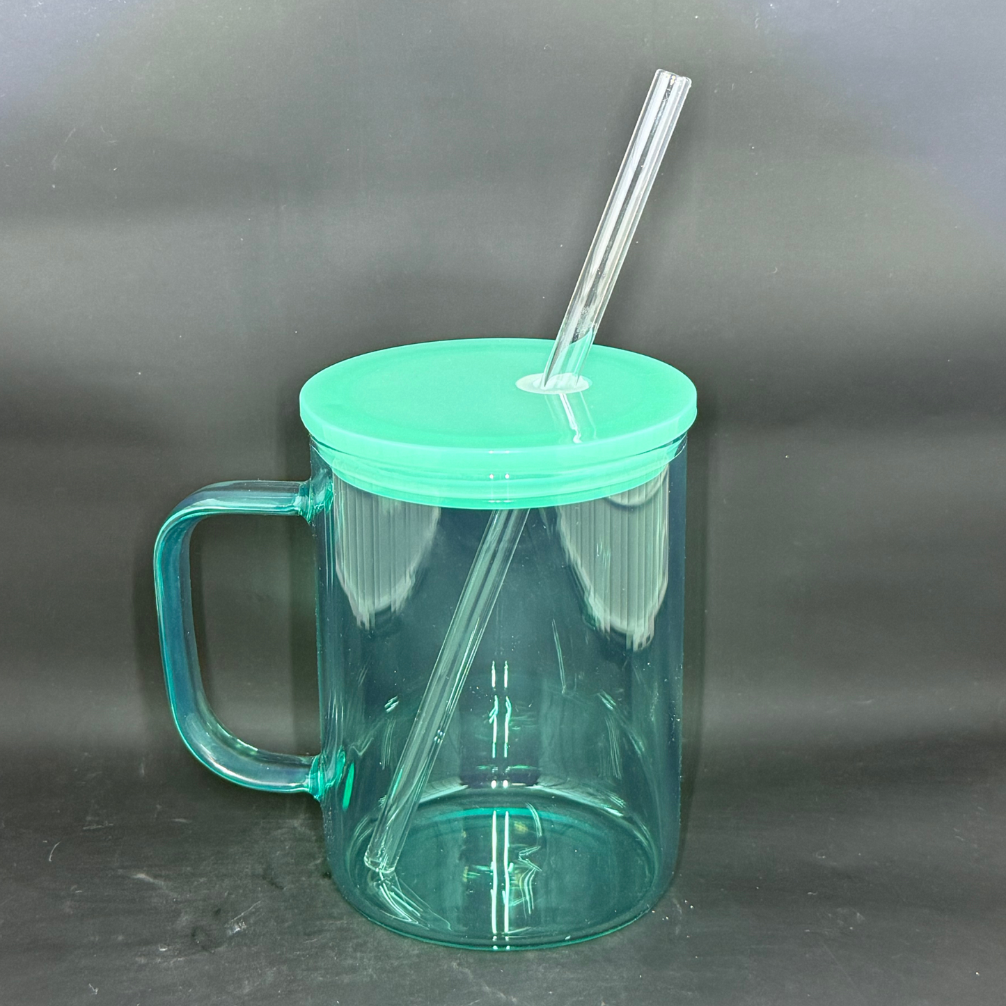 A translucent teal glass mug with a matching lid and straw against a dark background.