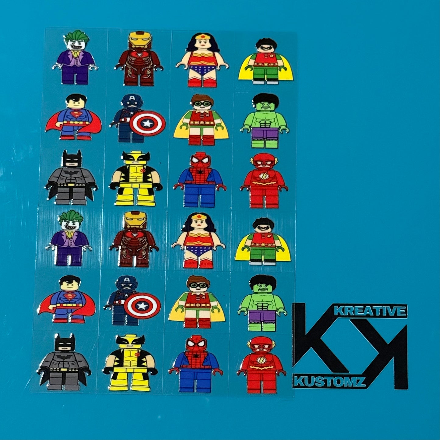 An A5 sheet of 24 precut UV DTF decals featuring various superhero and villain minifigure designs.