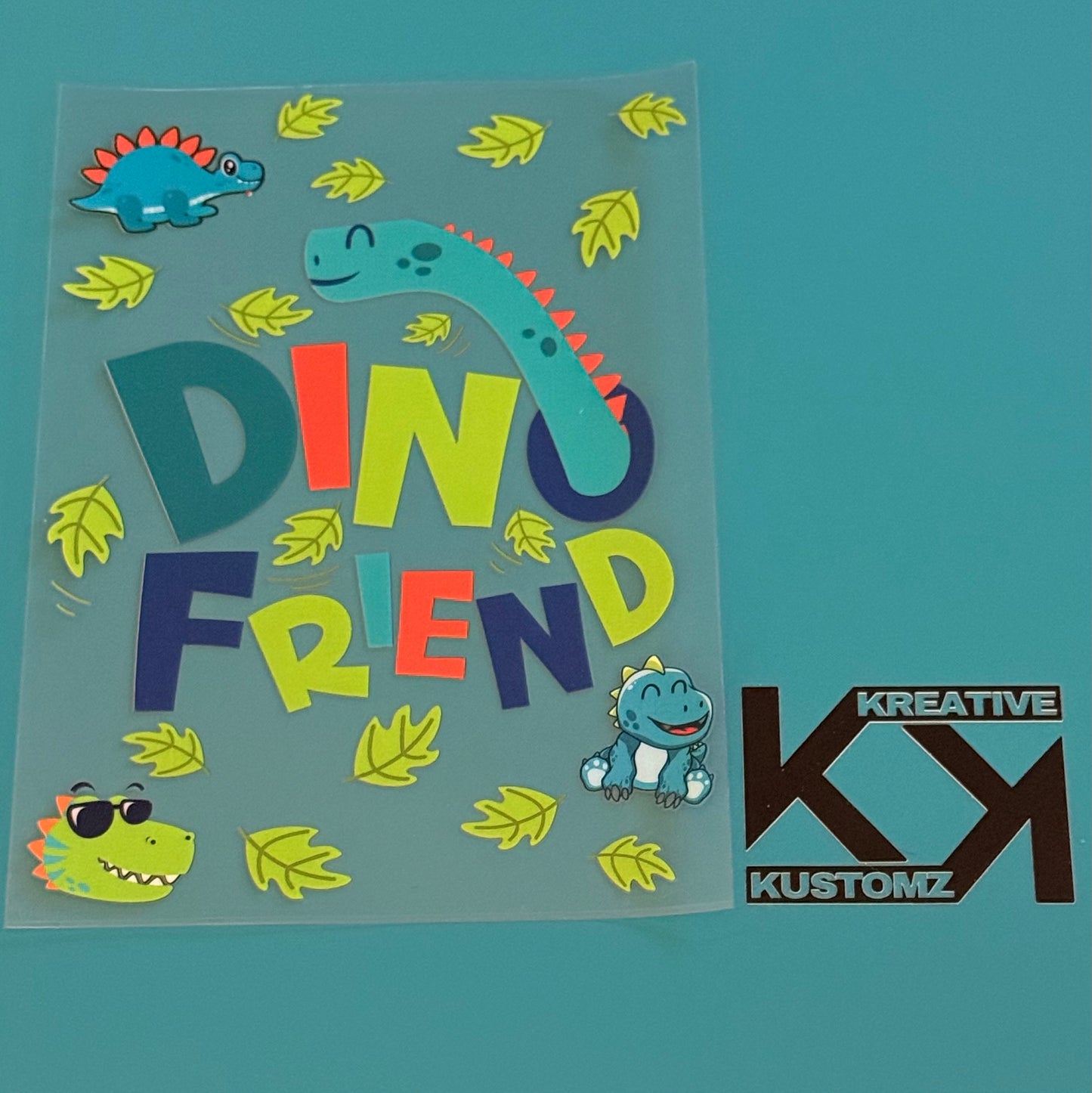 A Dino Friend UV-DTF notebook wrap featuring colorful dinosaurs and leaves on a clear sheet.