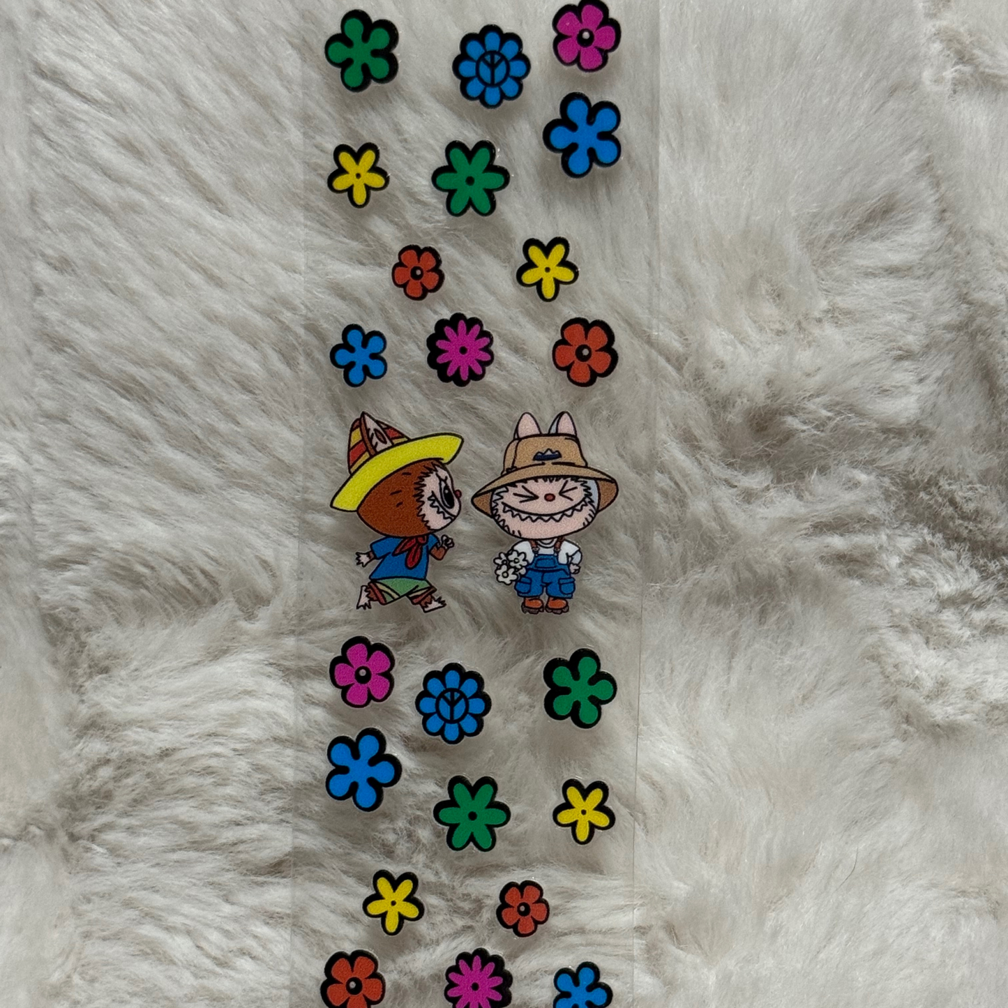 A clear adhesive pen wrap featuring two cartoon characters wearing hats surrounded by colorful flowers.