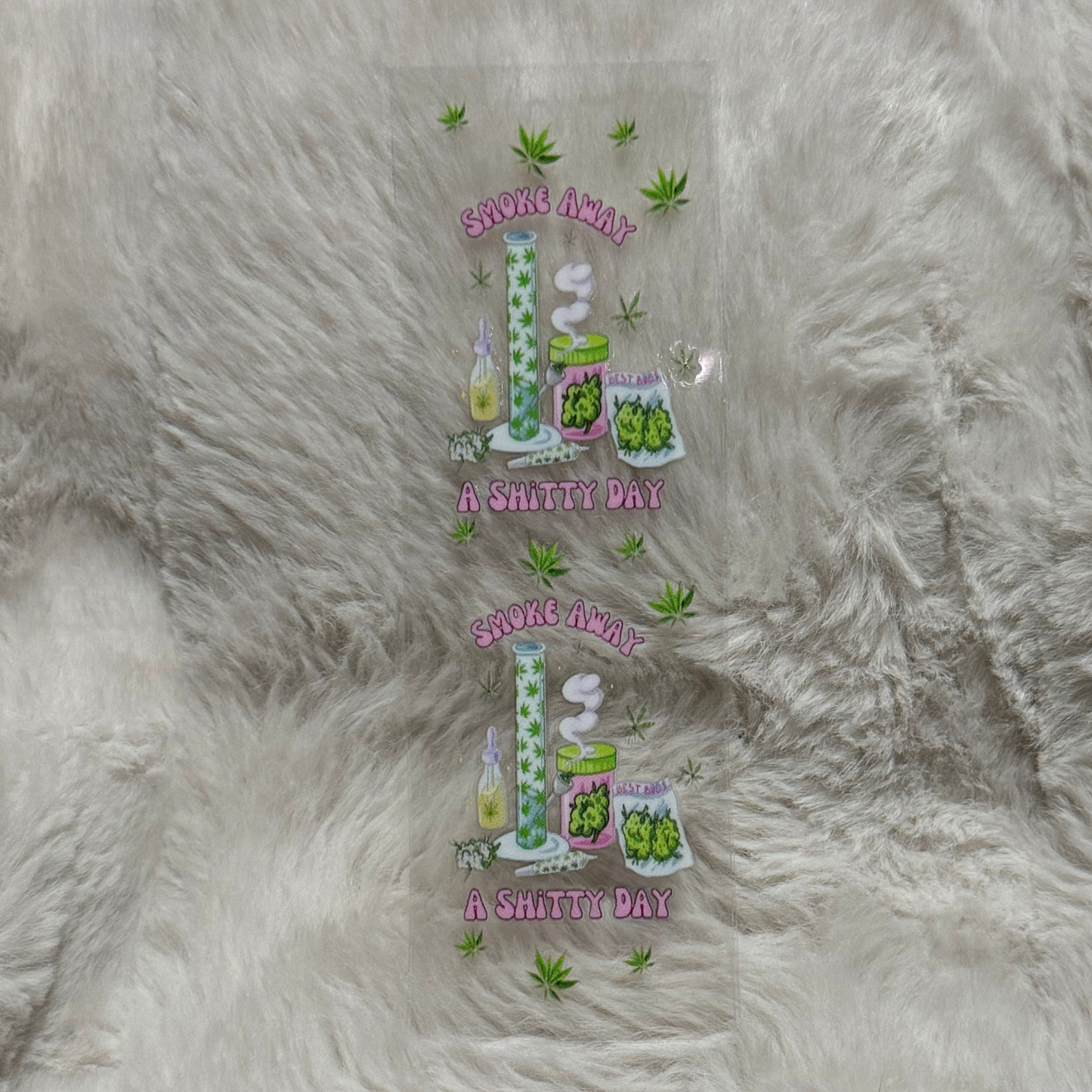 A clear UV DTF pen wrap featuring two identical cannabis-themed designs on a furry background.