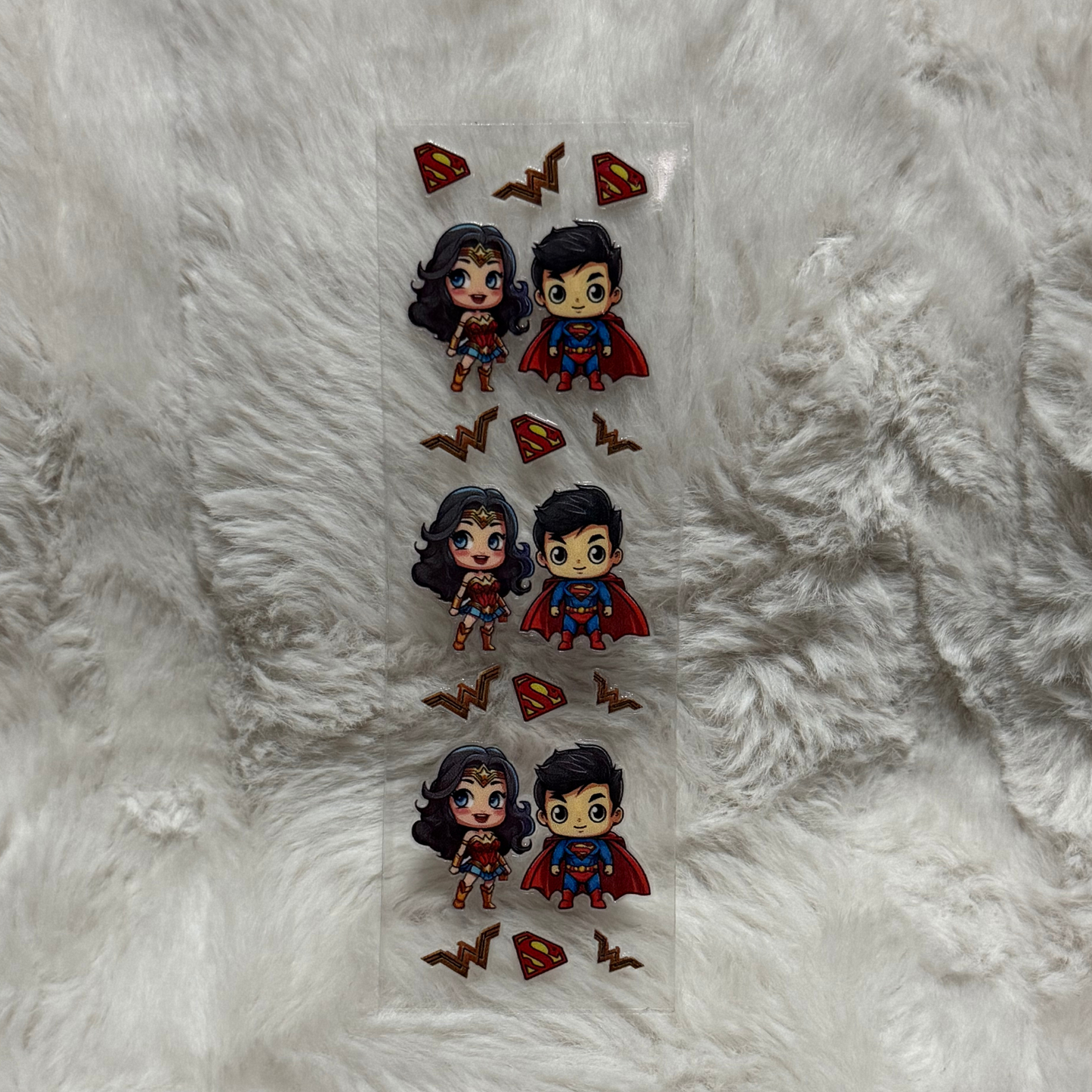 A rectangular UV DTF decal sheet featuring three repeating pairs of chibi Wonder Woman and Superman.