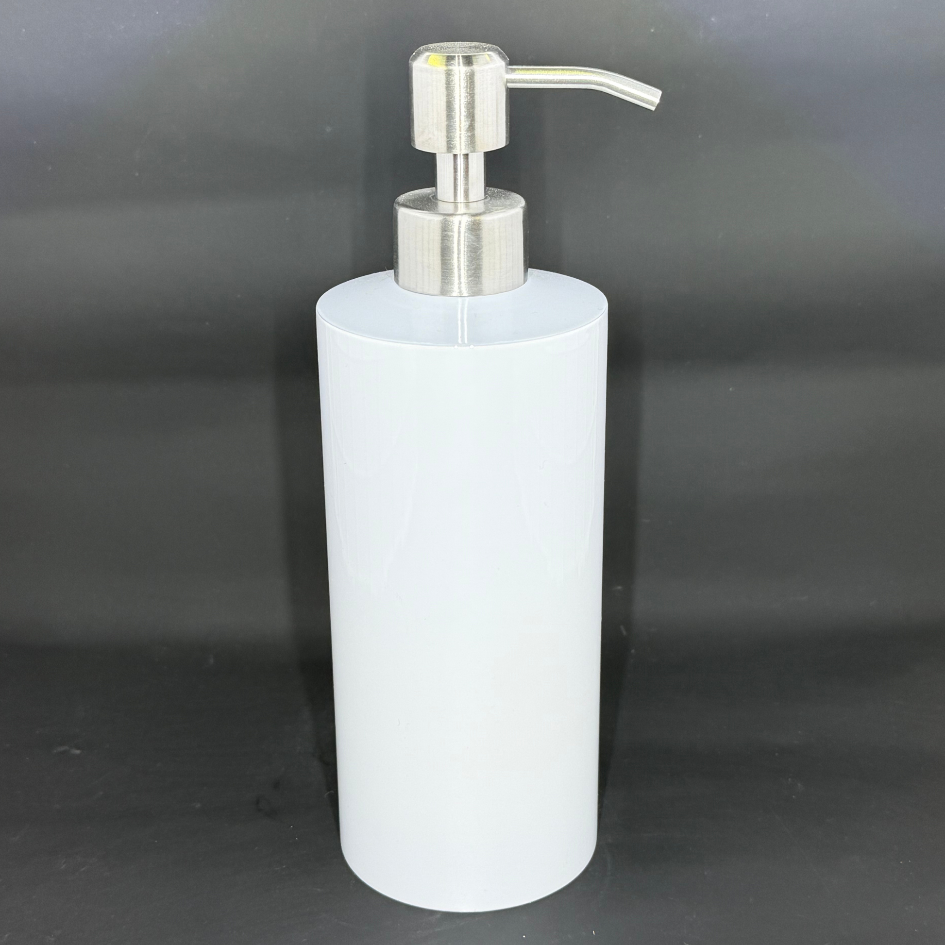 A white cylindrical soap dispenser with a silver pump mechanism against a black background.