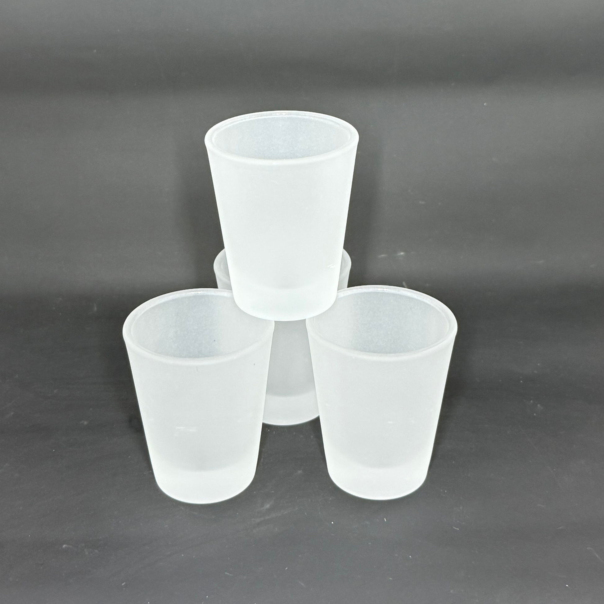 Three frosted matte glass shot glasses are arranged in a pyramid formation against a dark background.