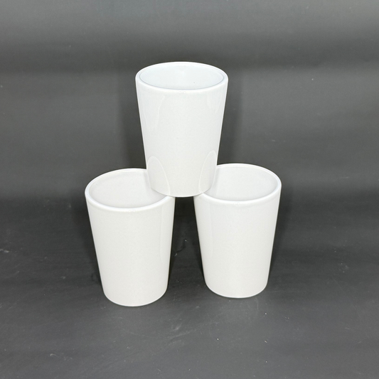 Three white ceramic shot glasses are arranged in a pyramid formation against a dark background.