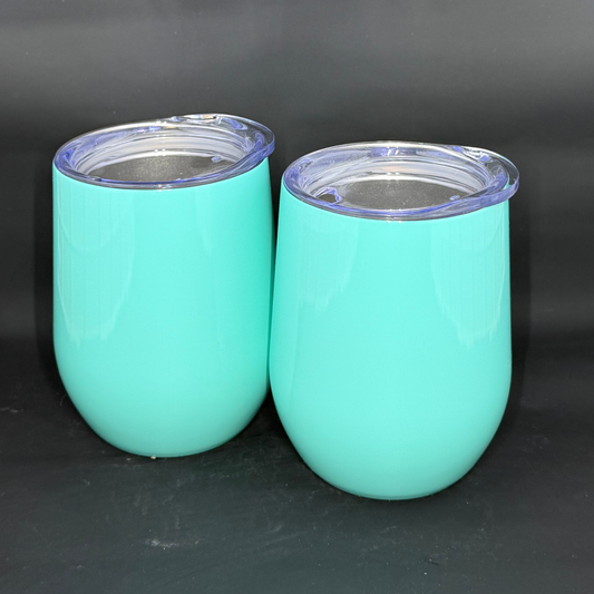 Two vibrant turquoise 12oz stemless wine tumblers with clear lids sit against a black background.