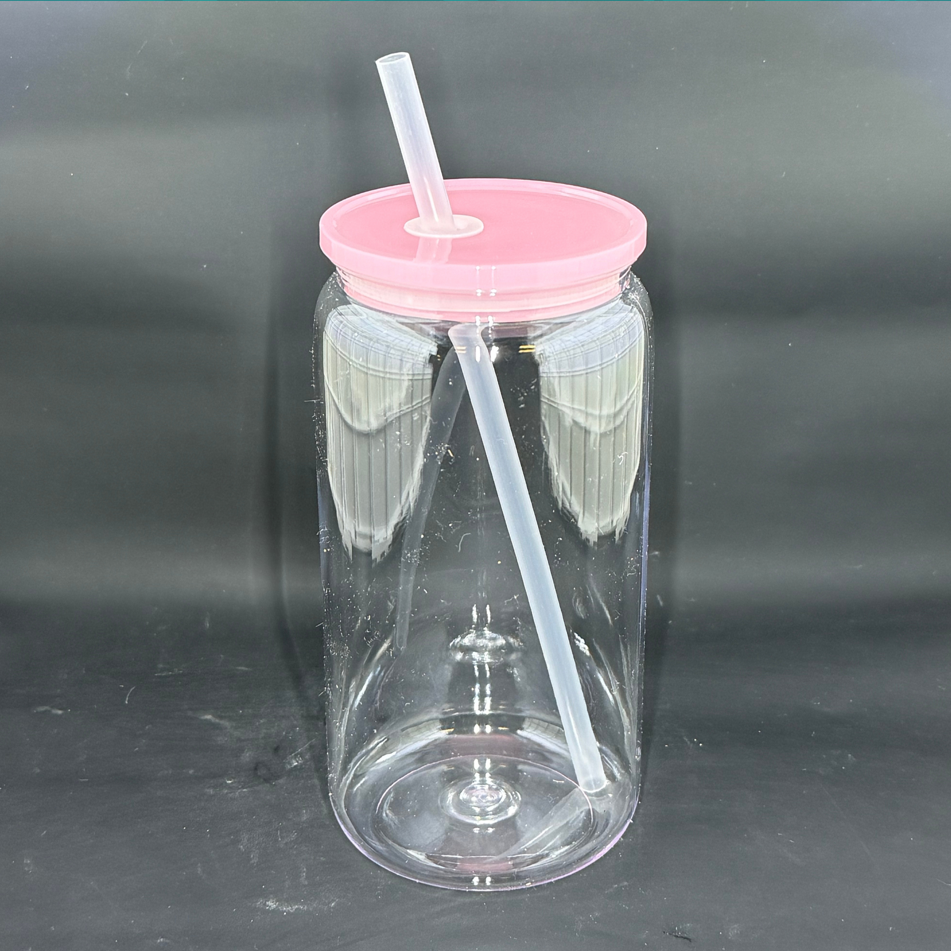 A clear 16oz acrylic beer can tumbler with a light pink lid and a matching straw.