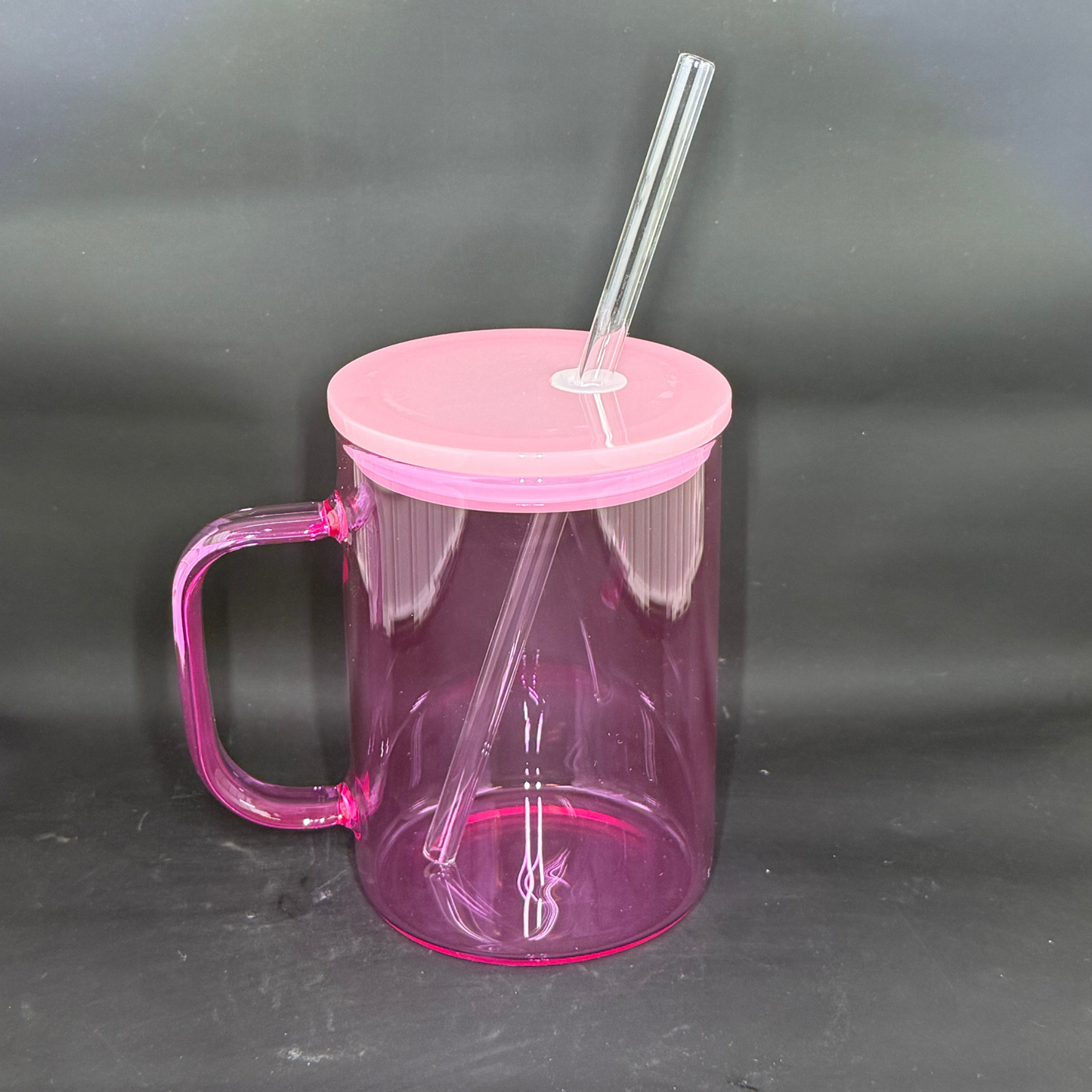 A translucent pink glass mug with a matching lid and clear straw against a dark background.