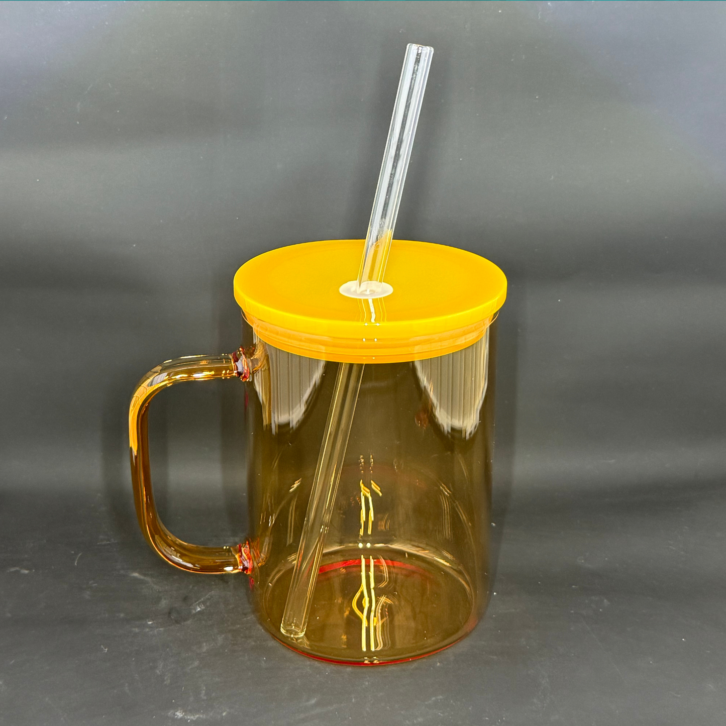 A translucent amber glass mug with a matching yellow lid and a clear glass straw.