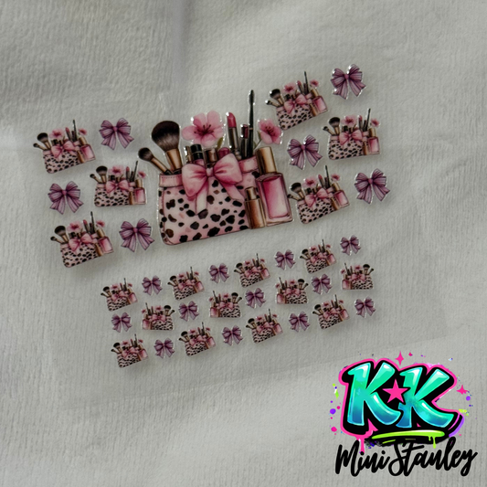 A sheet of UV DTF adhesive decals featuring pink makeup bags, brushes, and bows.