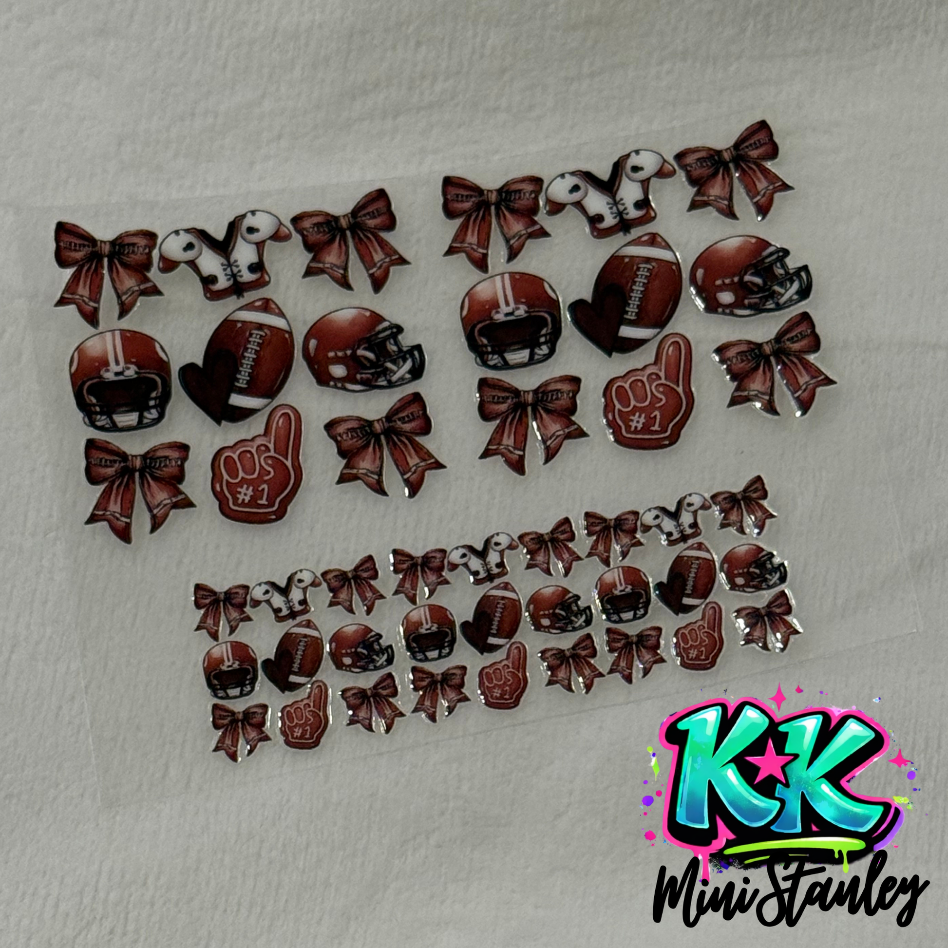 A sheet of football-themed UV DTF adhesive decals featuring helmets, bows, and foam fingers.