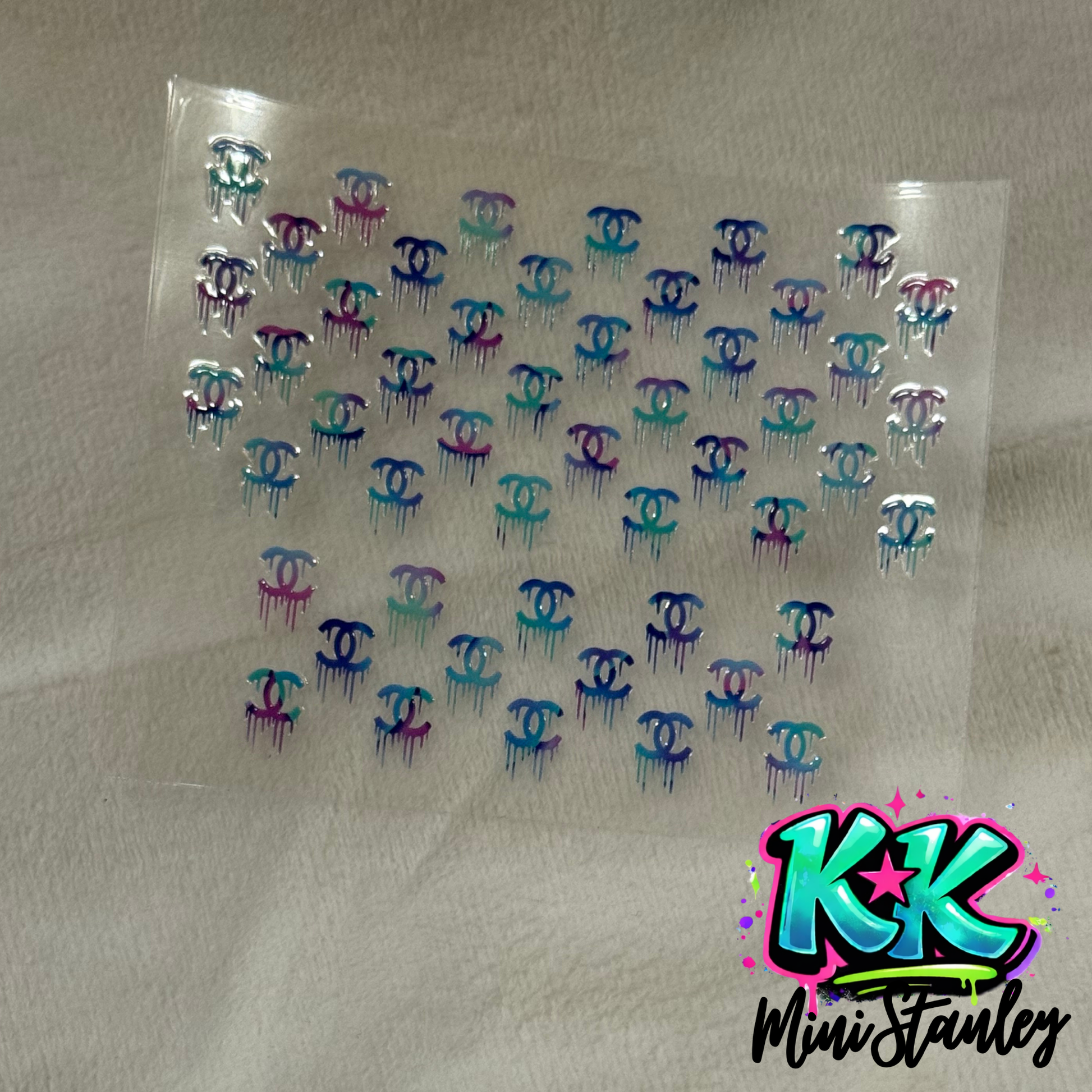 A sheet of UV DTF decals featuring multiple small, colorful, dripping Chanel-style logos.