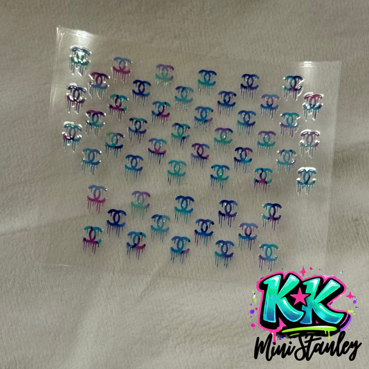 A sheet of UV DTF decals featuring multiple small, colorful, dripping Chanel-style logos.