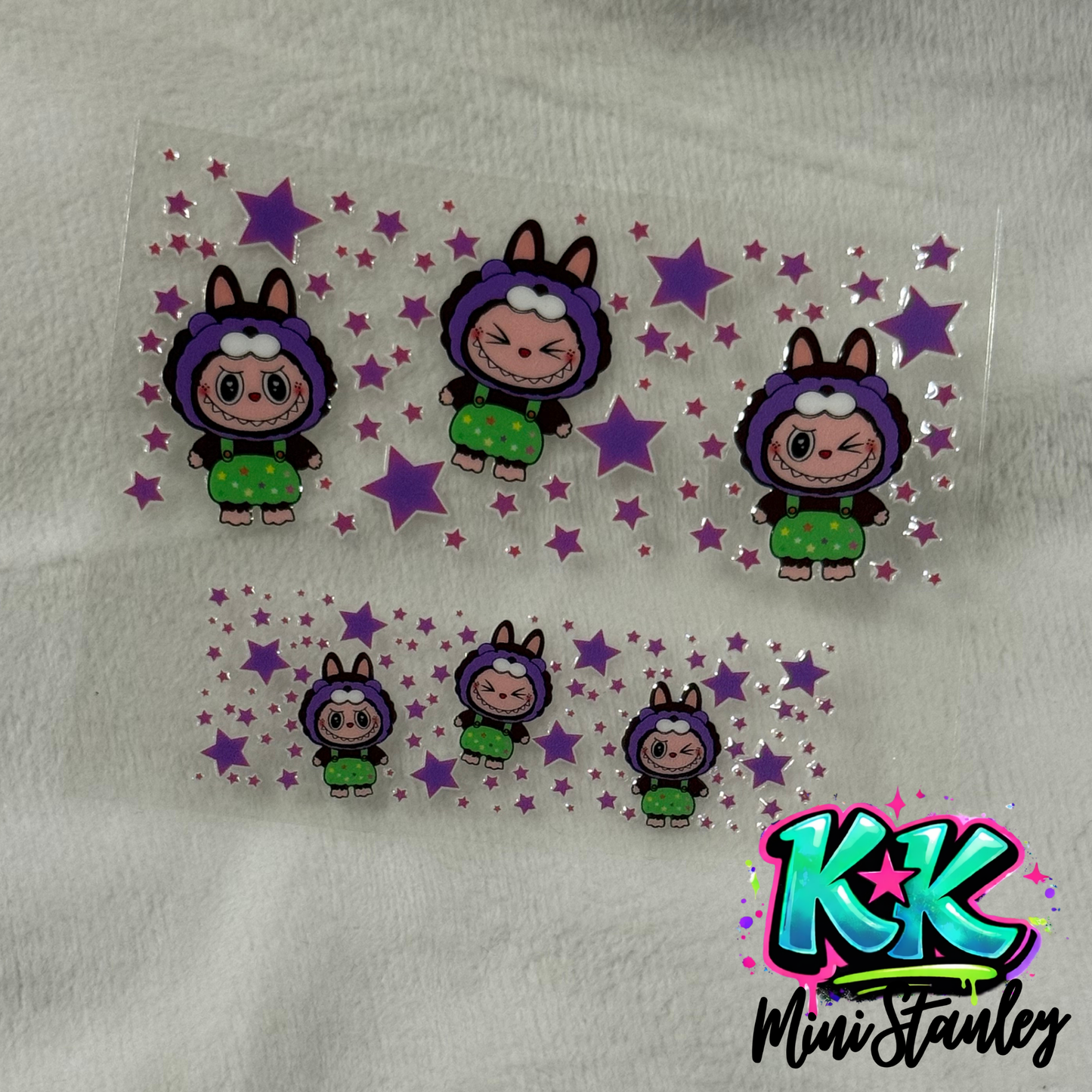 Two sheets of UV DTF adhesive decals featuring cartoon characters in purple hoods and star accents.