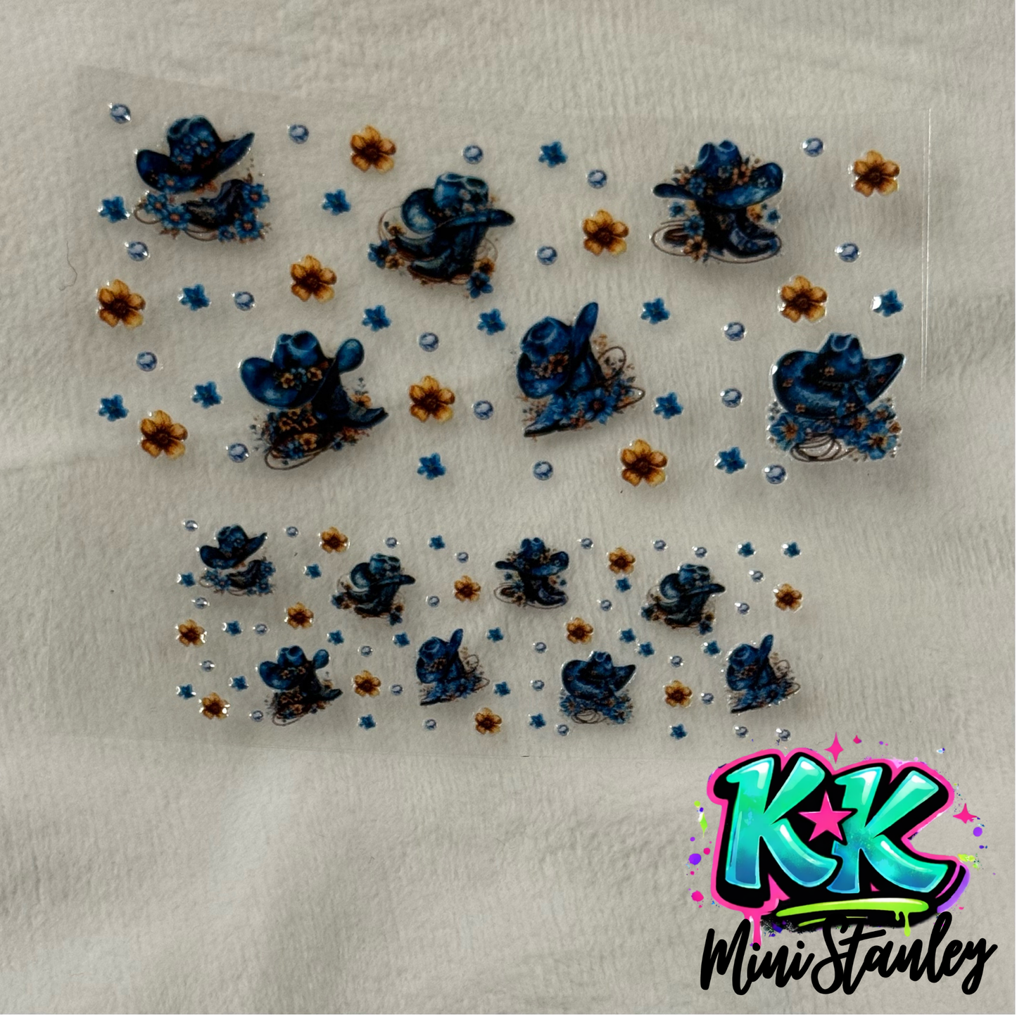 A UV DTF adhesive wrap featuring blue cowboy hats and small flowers for mini cups or keychains.