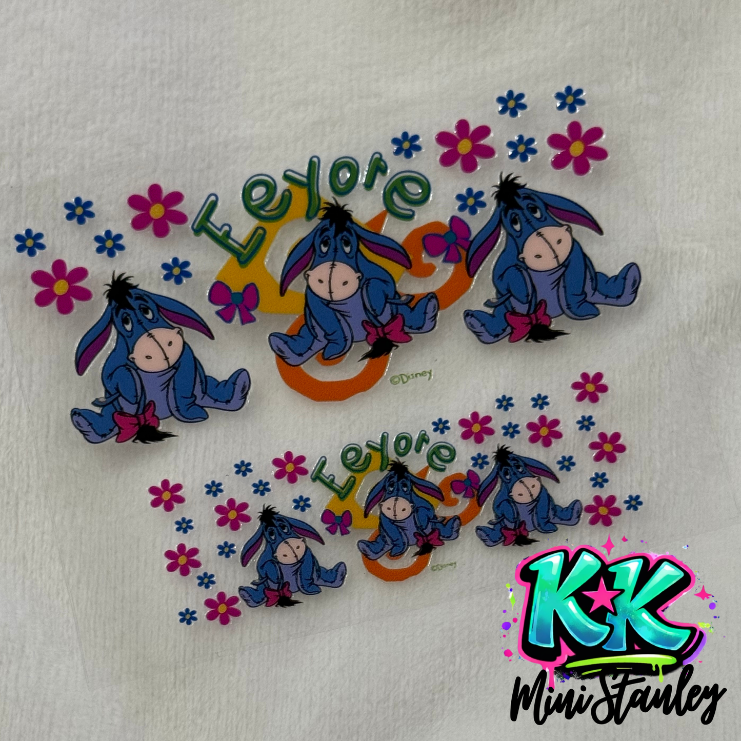 Two UV DTF adhesive sheets featuring Eeyore, flowers, and the name Eeyore in green text.