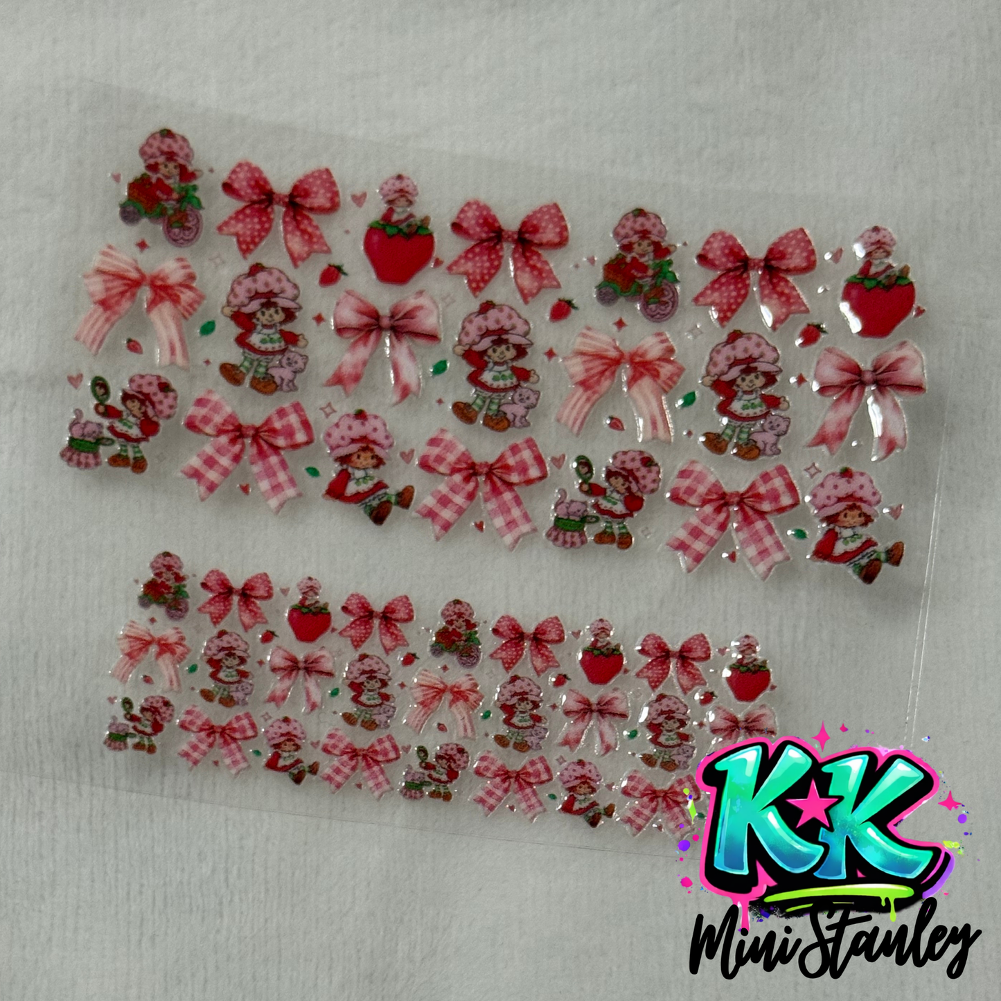 Two sheets of Strawberry Shortcake themed UV DTF adhesive transfers with bows and strawberries.