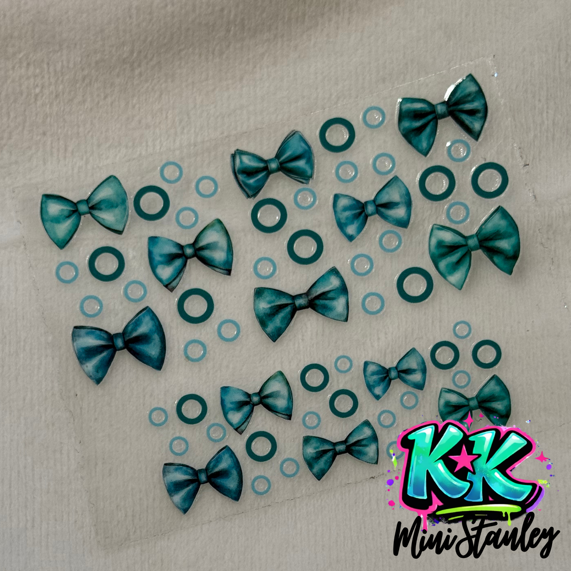 A sheet of UV DTF adhesive decals featuring teal bows and small circles.