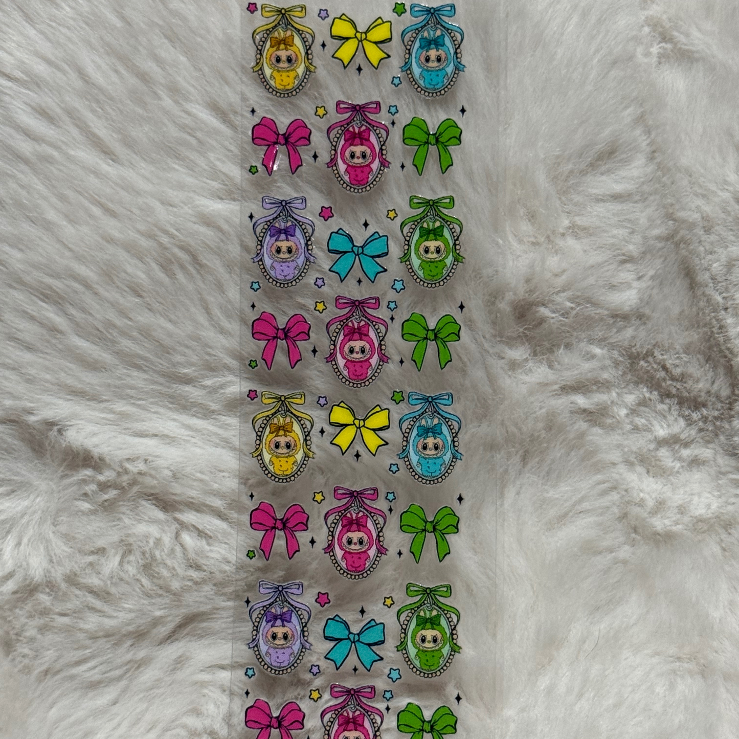 A clear adhesive pen wrap featuring a repeating pattern of colorful bows and framed baby characters.