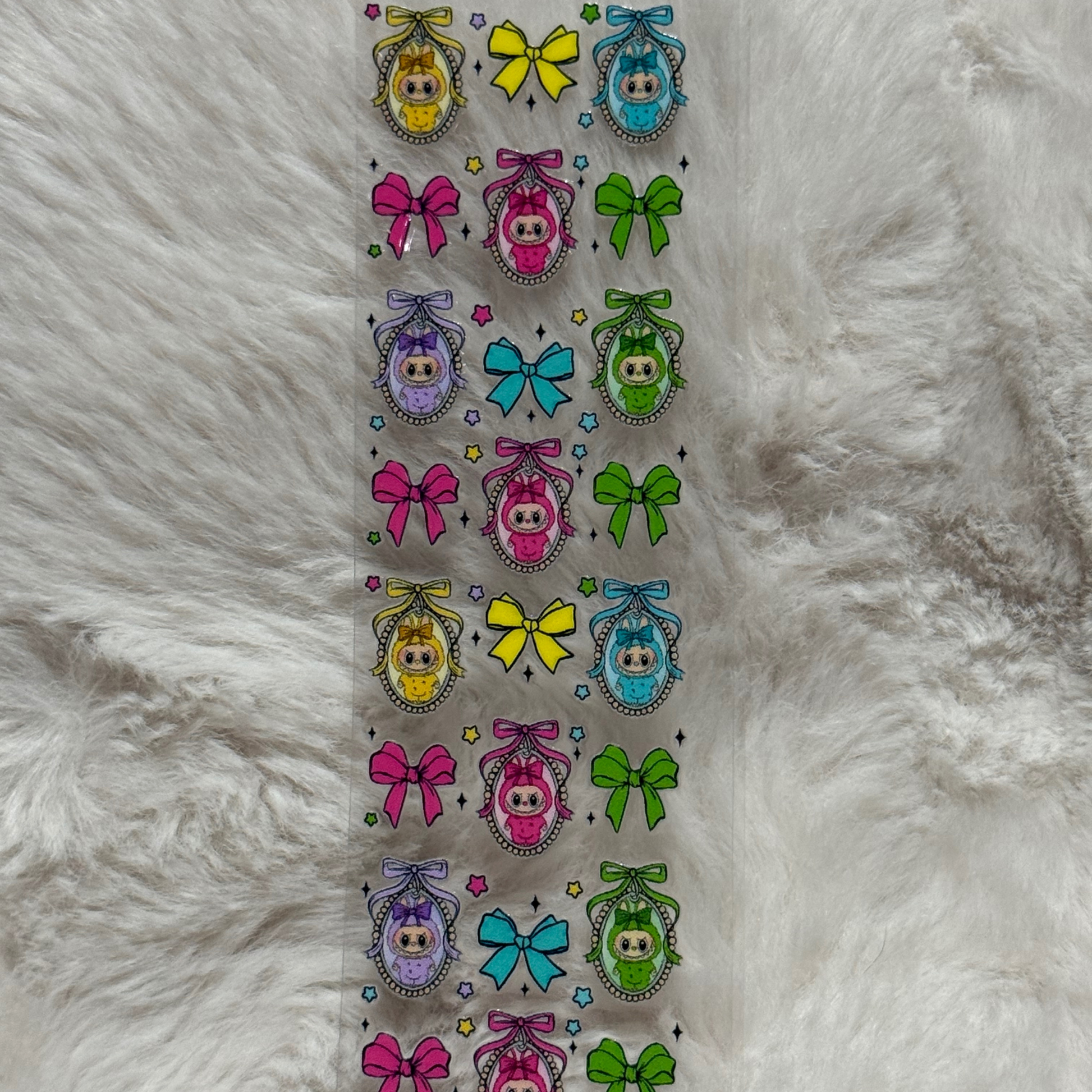 A clear adhesive pen wrap featuring a repeating pattern of colorful bows and framed baby characters.