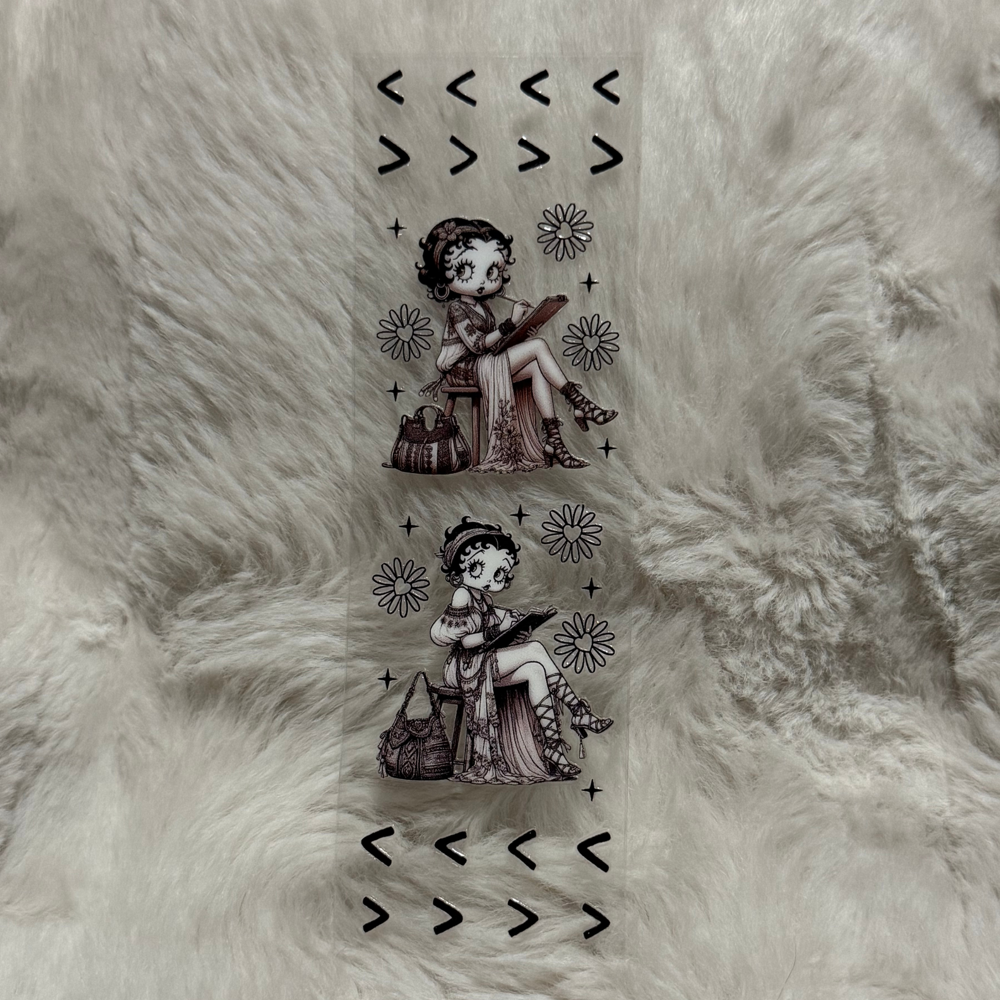 A clear adhesive pen wrap featuring two illustrations of Betty Boop sketching with floral accents.