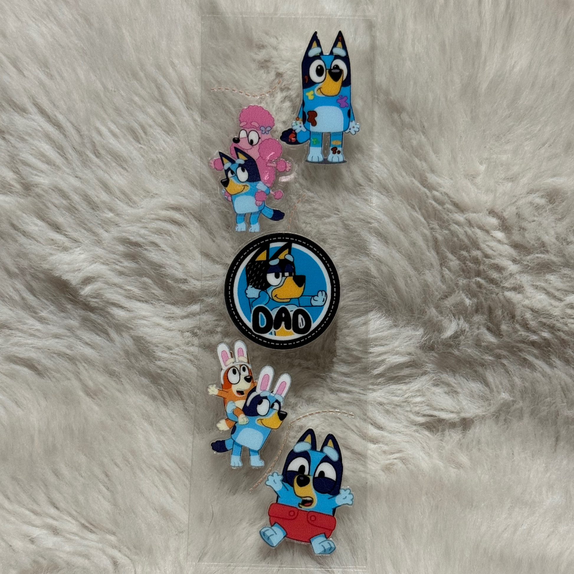 A clear adhesive pen wrap featuring various Bluey character designs on a white faux fur background.
